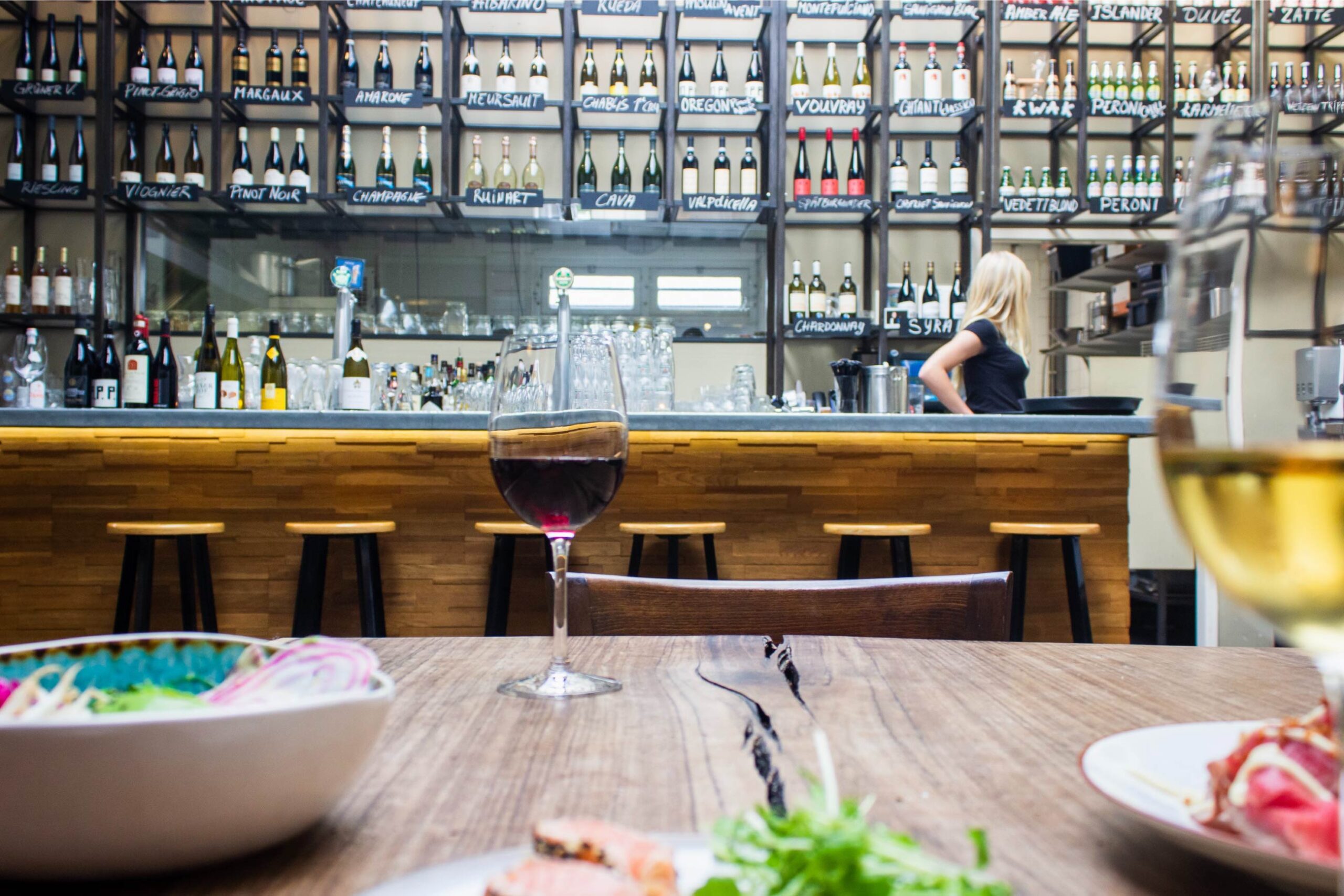 Barra de bar o restaurante con copas de vino sin alcohol y varias botellas de vino sin alcohol al fondo